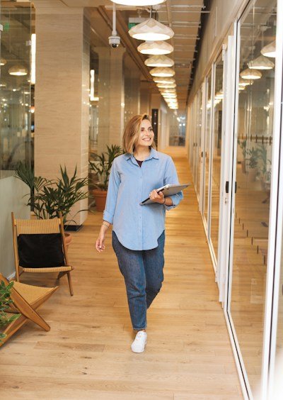 woman in blue dress shirt and blue denim jeans standing beside brown wooden chair